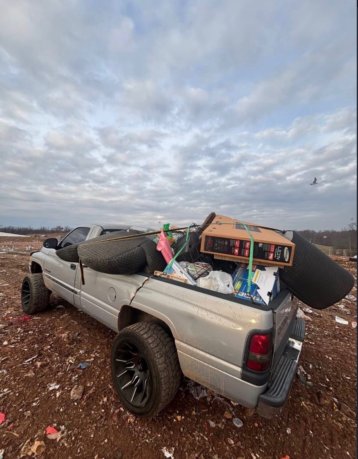 Silver pickup loaded with household items and furniture at a disposal site